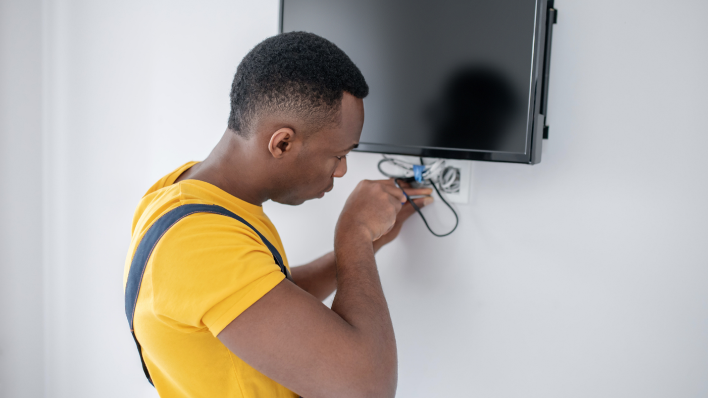 A man adjusts the wires from a television mounted on a wall.