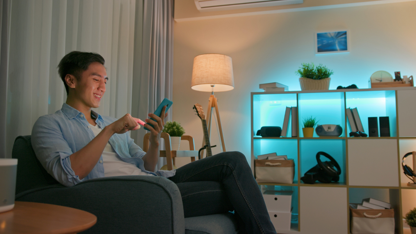 A man uses his smartphone in his living room, behind him LED lights glow blue.