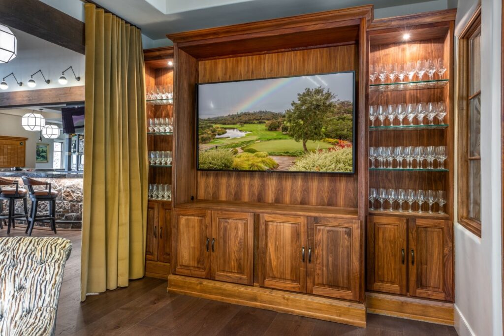 A large cabinet with a flatscreen TV and many wine glasses on either side.