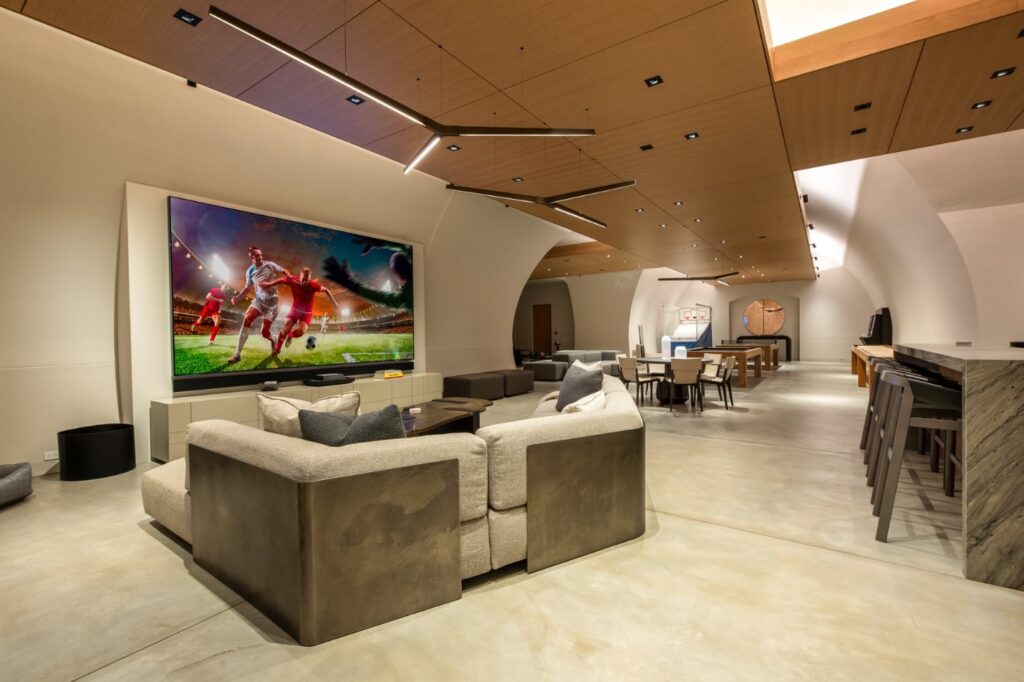 A large living room with a large screen TV and in-ceiling lighting.